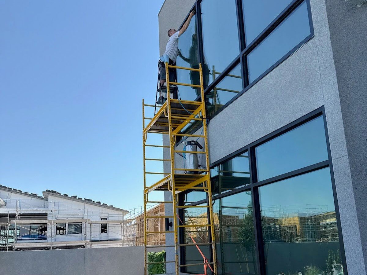 A technician on a scaffold applying film to a two-story window